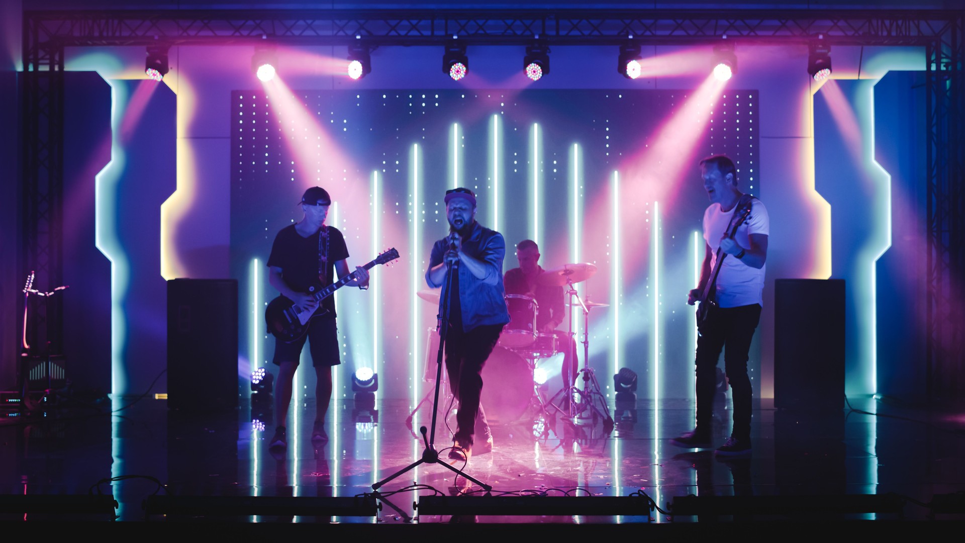 Four Man Rock Band with Lead Singer, Guitarists, Bassist and Drummer Performing at a Concert in a Night Club. Live Music Party in Front of Bright Colorful Strobing Lights on Stage.